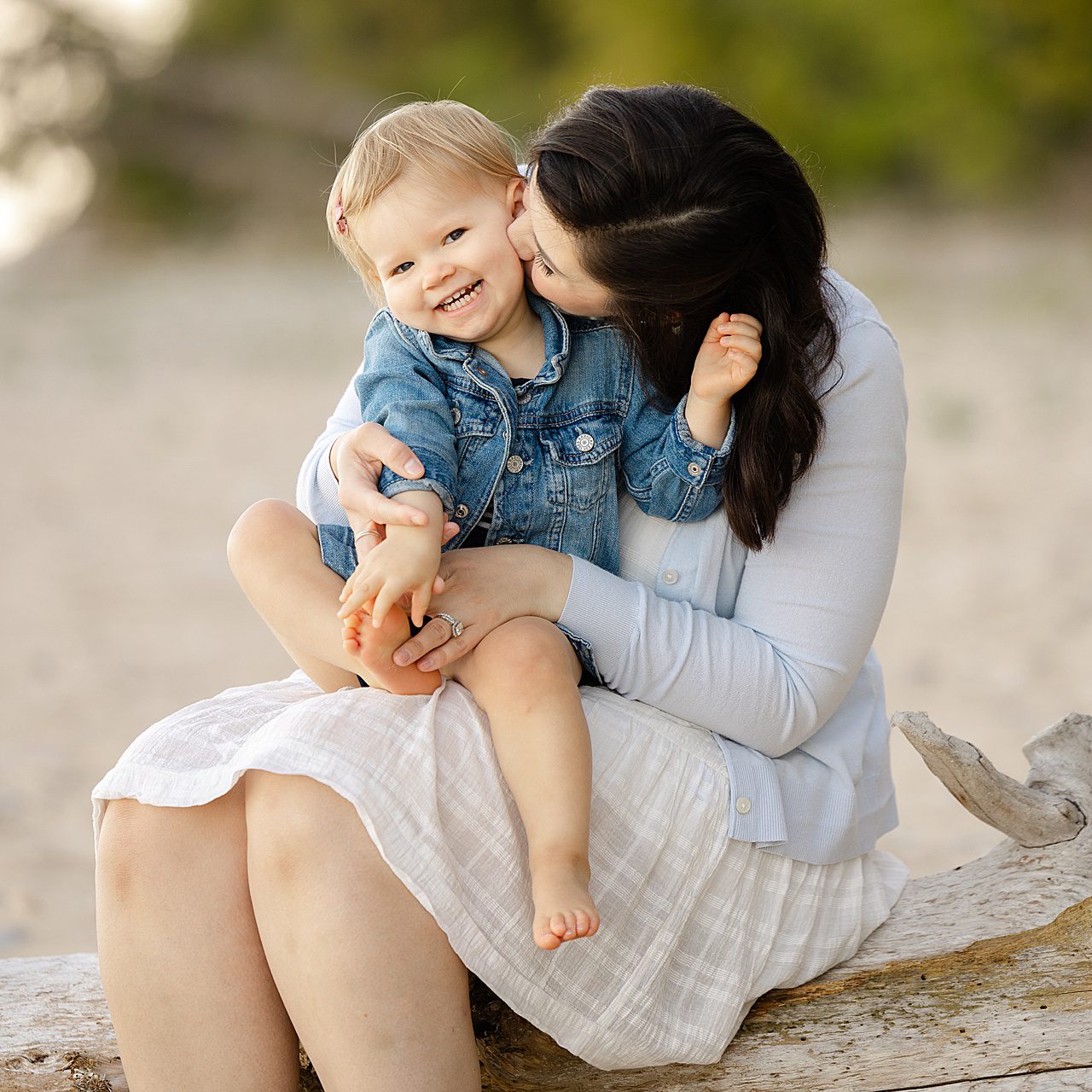 Family photo of a mother kissing her daughter on a beach in michigan