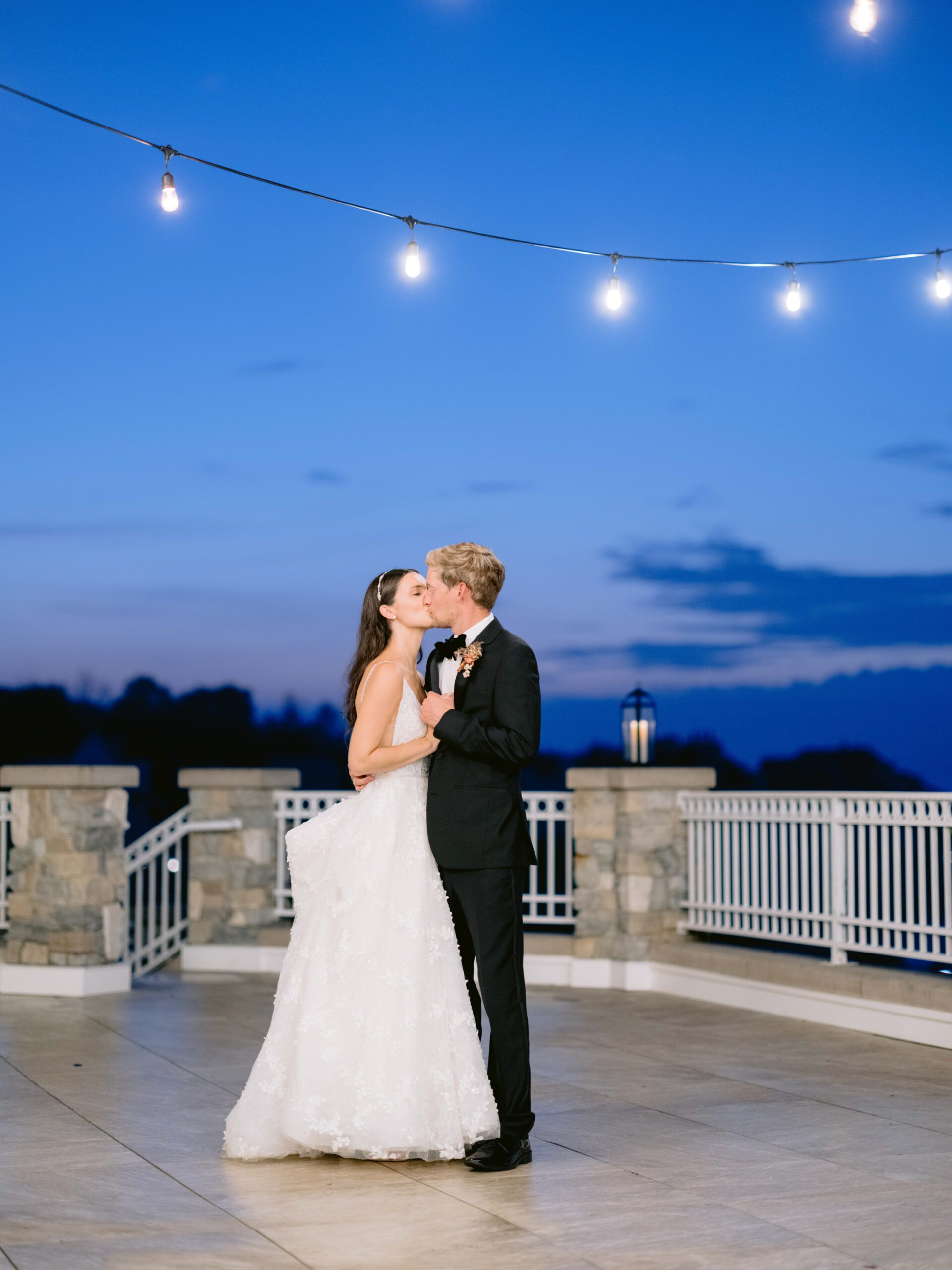 Newlyweds kiss under string lights on a stone porch in Petoskey Michigan