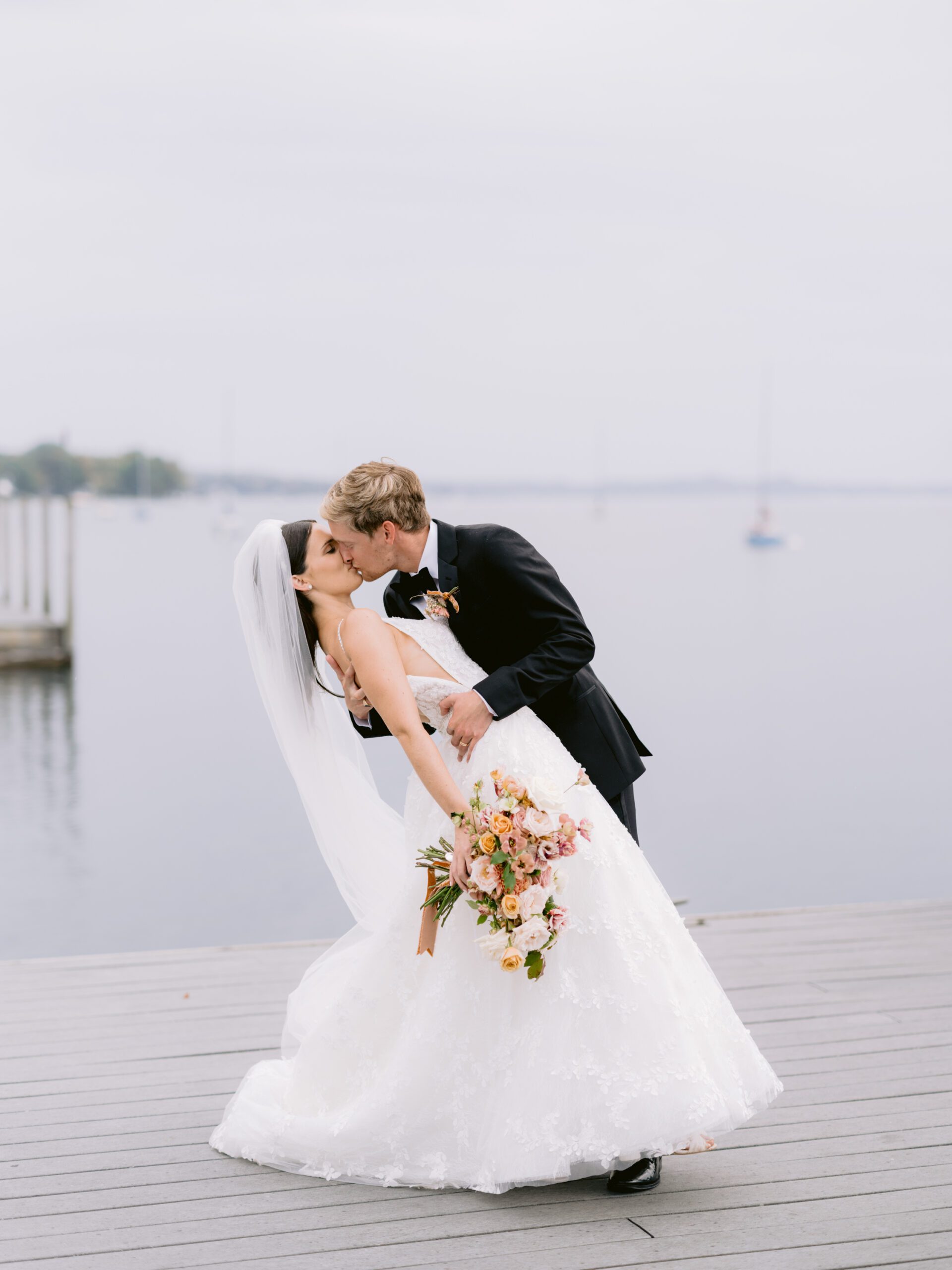 A bride and groom kiss on a dock in Northern Michigan in front of sailboats