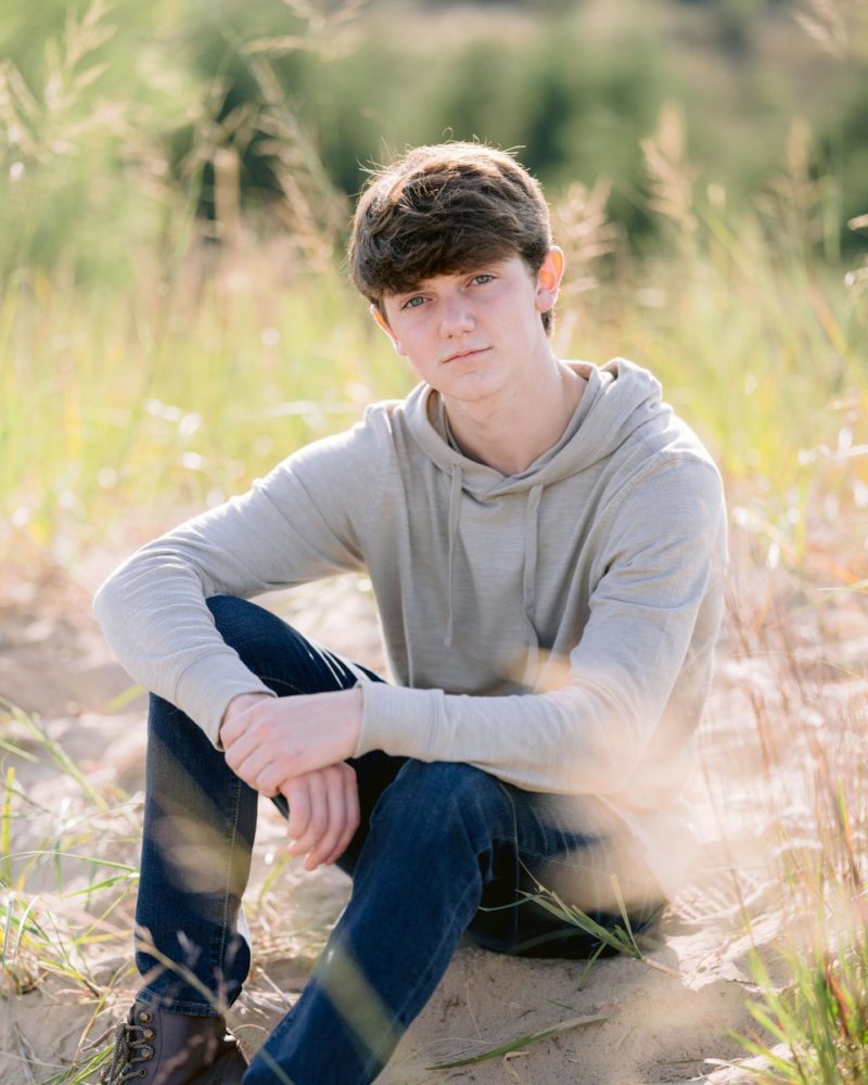 a young man sits in the sand for portrait photography