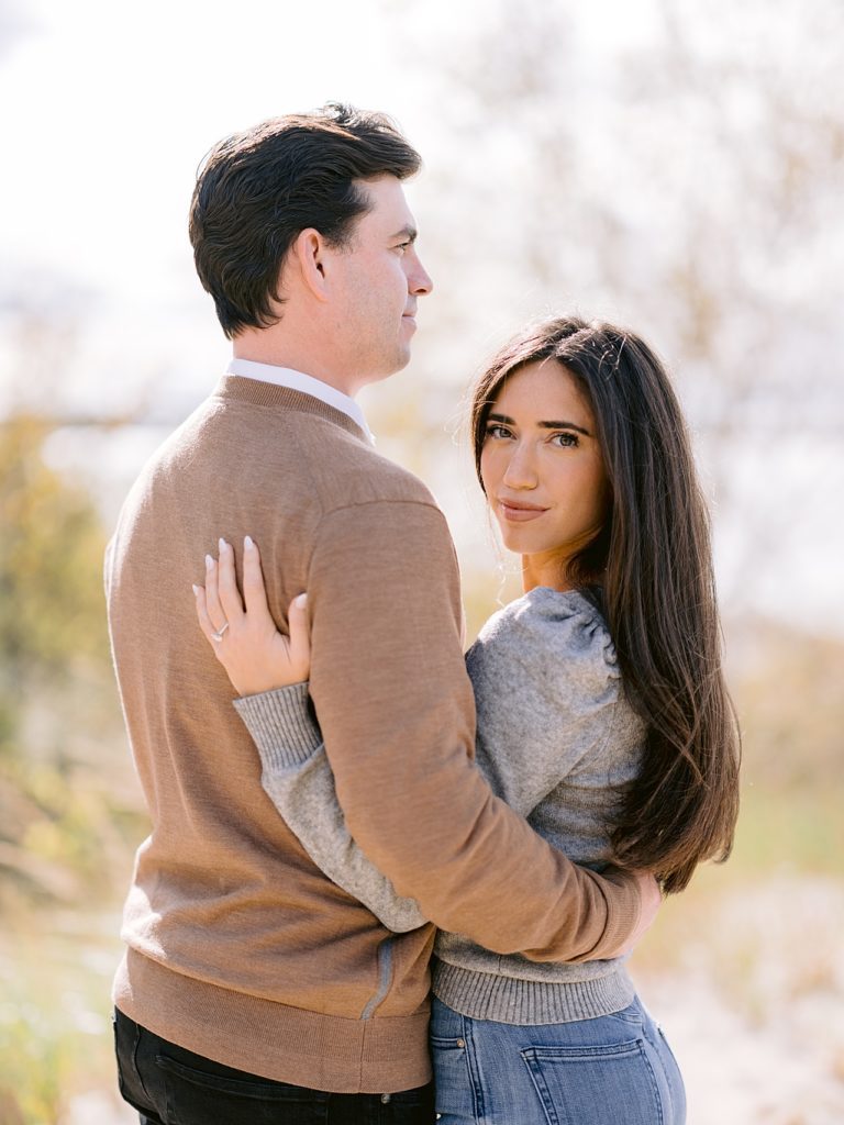 A woman looks over her fiancé's shoulder for a fall engagement in michigan