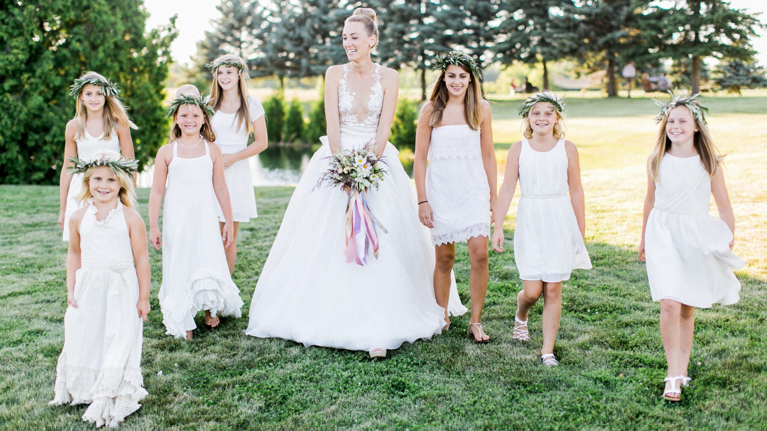 A bride walks across grass with her flower girls for traverse city wedding photographer
